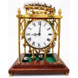 A brass falling ball clock with heavy polished steel ball bearings under polished wood and glazed