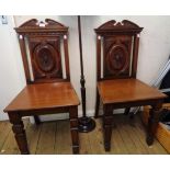 A pair of late Victorian walnut framed hall chairs with decorative applied moulding to backs, set on