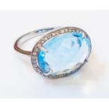 A marked 9k white metal ring, set with large oval topaz within a diamond encrusted border
