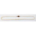 A single string graduated cultured pearl necklace with 9ct. gold seed pearl and garnet clasp