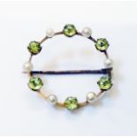 A yellow metal open circular brooch, set with alternating peridot and seed pearls