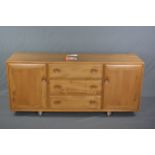AN ERCOL WINDSOR ELM SIDEBOARD, with three long drawers and two cupboard doors on casters,