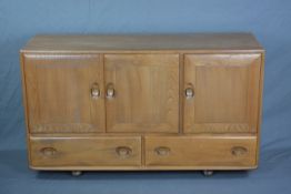 AN ERCOL WINDSOR ELM SIDEBOARD, with three cupboard doors, with central interior drawer and