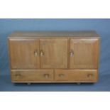 AN ERCOL WINDSOR ELM SIDEBOARD, with three cupboard doors, with central interior drawer and