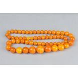 AN ORANGE PLASTIC BEAD NECKLACE, imitating amber, round graduated beads, approximate length 26