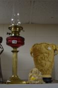 A VICTORIAN BRASS BASED COLUMN OIL LAMP, cranberry glass reservoir with chimney, lacks shade,