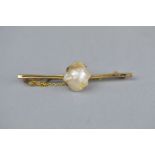 AN EARLY 20TH CENTURY BAROQUE PEARL 9CT GOLD BAR BROOCH, the large central pearl measuring