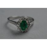 A MODERN EMERALD AND DIAMOND OVAL CLUSTER RING, emerald measuring approximately 7mm x 5mm, estimated