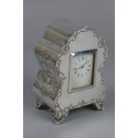 A LATE VICTORIAN/EDWARDIAN SILVER BOUDOIR CLOCK, the front with foliate scroll outline, the sides