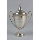AN EDWARDIAN SILVER TWIN HANDLED TROPHY CUP AND COVER, knop finial above a dome, the cup engraved '