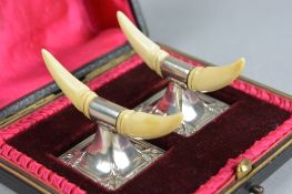 A CASED PAIR OF EDWARDIAN SILVER AND IVORY KNIFE RESTS, the rests shaped as a pair of horns over