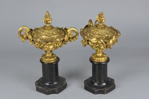 A PAIR OF LATE 19TH CENTURY GILT METAL TWIN HANDLED URNS AND COVERS, cast with foliage and berries