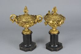 A PAIR OF LATE 19TH CENTURY GILT METAL TWIN HANDLED URNS AND COVERS, cast with foliage and berries