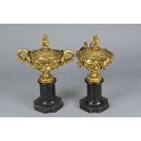 A PAIR OF LATE 19TH CENTURY GILT METAL TWIN HANDLED URNS AND COVERS, cast with foliage and berries