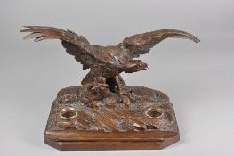 A LATE 19TH CENTURY BLACK FOREST DESK STAND, carved as an Eagle with wings outstretched on a rocky