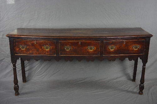 A GEORGE III OAK DRESSER, fitted with three deep drawers above a wavy apron, on front baluster