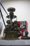 A VICTORIAN STYLE OIL LAMP, converted to electric, depicting three seated cherubs, height of base