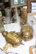 A PAIR OF BRASS WALL MOUNT OIL LAMPS WITH FOUR VARIOUS GLASS CHIMNEYS, together with a brass