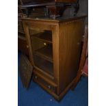 AN ERCOL GOLDEN DAWN GLAZED SINGLE DOOR CABINET, with adjustable shelving above a single drawer,