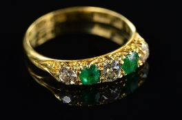 AN 18CT EDWARDIAN EMERALD AND DIAMOND HALF HOOP RING, carved scroll sides and settings, three old