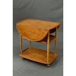 A BLONDE ERCOL ELM DROP-LEAF THREE TIER TEA TROLLEY, the rounded drop leaves to form an oval,
