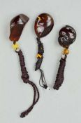 THREE BURMESE AMBER PENDANTS, the first carved to depict fruit, the other two polished amber pieces,