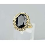 A 9CT GOLD SAPPHIRE AND DIAMOND CLUSTER RING, the central stone on oval shape sapphire within a