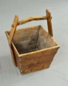 A 19TH CENTURY WOODEN LOG BASKET, of square tapering form, fitted with a pegged handle on shaped