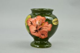 A SMALL MOORCROFT POTTERY FOOTED VASE, 'Hibiscus' pattern on green ground, impressed mark to base,