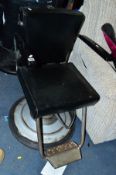 A BLACK UPHOLSTERED BARBERS CHAIR (missing headrest)