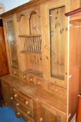 A PINE KITCHEN DRESSER, with shelves and spindled plate rack central to two glazed doors above eight