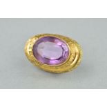 AN AMETHYST BROOCH, oval amethyst measuring 19.0mm x 15.2mm, rub over set to textured stepped mount,