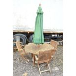 AN OCTAGONAL TEAK GARDEN TABLE, with four folding chairs and a parasol (6)