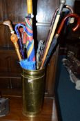 A BRASS UMBRELLA STAND, with contents including a pewter topped cane, walking sticks, etc