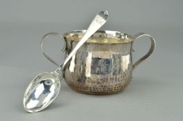 A SILVER EDWARDIAN PORRINGER AND SPOON, the double handled porringer of hammered design with