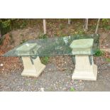 A GLASS TOPPED GARDEN TABLE, with two stone effect plastic column supports, approximately 202cm x