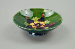 A MOORCROFT POTTERY FOOTED TRINKET DISH, 'Columbine' pattern on green ground, paper label to base,