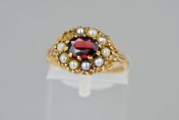 A 9CT GOLD GARNET AND PEARL CLUSTER RING, the central oval garnet within a split pearl surround (