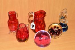 SIX PIECES OF GLASSWARE, to include three cranberry coloured jugs, Mdina paperweight and two