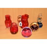 SIX PIECES OF GLASSWARE, to include three cranberry coloured jugs, Mdina paperweight and two