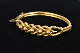 AN EARLY 20TH CENTURY 9CT GOLD HINGED BANGLE, the front an openwork interwoven design with bead