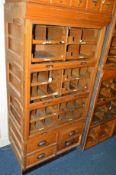 A TALL GOLDEN OAK HABERDASHERY CABINET comprising of three glazed disappearing flaps, revealing