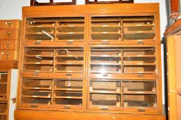 A GOLDEN OAK HABERDASHERY CABINET comprising of six glazed disappearing flap doors revealing