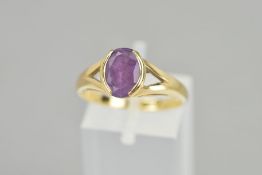 A 9CT GOLD AMETHYST RING, the oval amethyst within a part collet setting to the bifurcated