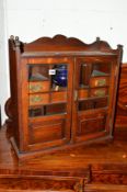 AN EDWARDIAN BEVELLED GLAZED TWO DOOR SMOKERS CABINET, the interior with seven various drawers and