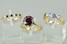 THREE 9CT GOLD RINGS to include a circular garnet ring, a tanzanite four stone ring and a sapphire
