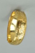 A 9CT GOLD HINGED BANGLE, the front half engraved with scrolling acanthus leaf decoration to the