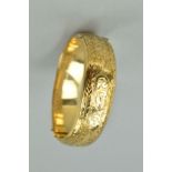 A 9CT GOLD HINGED BANGLE, the front half engraved with scrolling acanthus leaf decoration to the