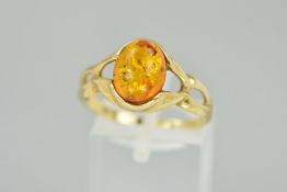 A 9CT GOLD MODIFIED AMBER RING, designed as an oval modified amber cabochon to the tapered