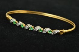 A 9CT GOLD EMERALD AND DIAMOND BANGLE, designed as five circular emeralds interspaced by leaf
